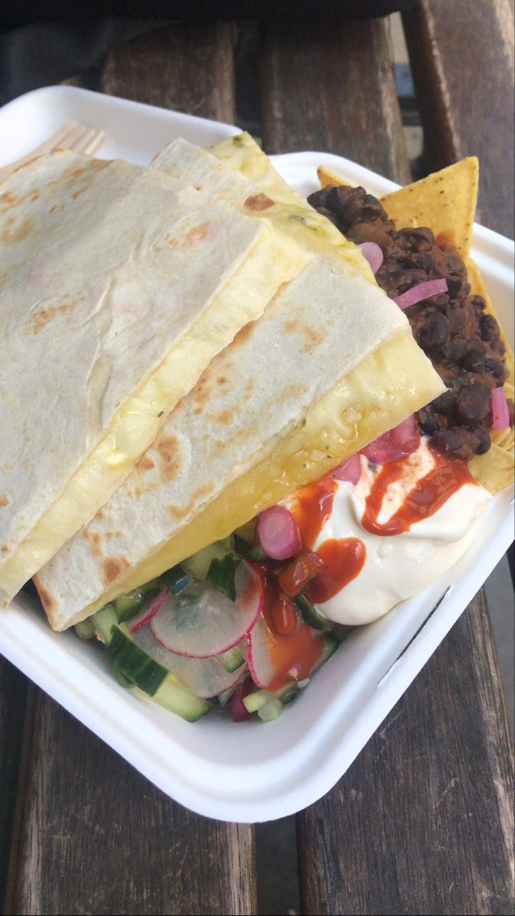 A grilled quesadilla with salad and sauce in a takeaway box